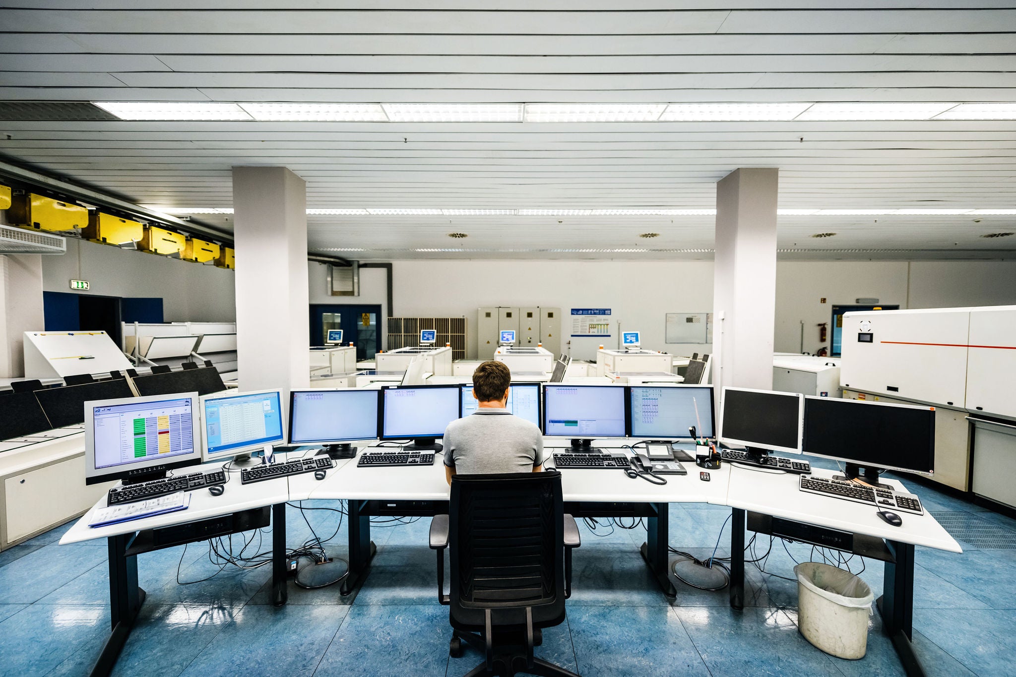 Back shot of an engineer sitting on a desk and working on computers in a large clean control room of a modern printery