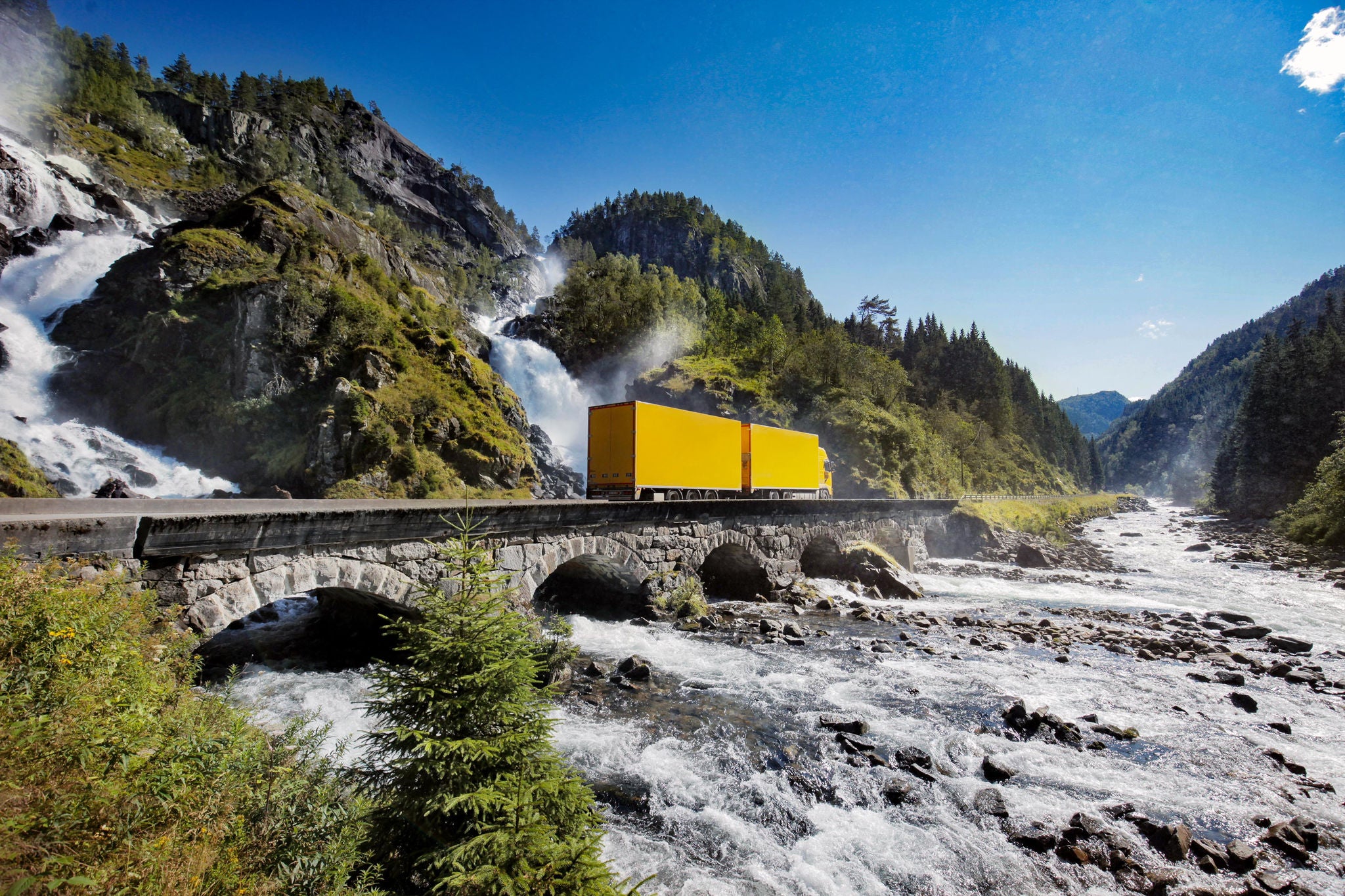 Yellow truck crossing bridge by waterfall in norway