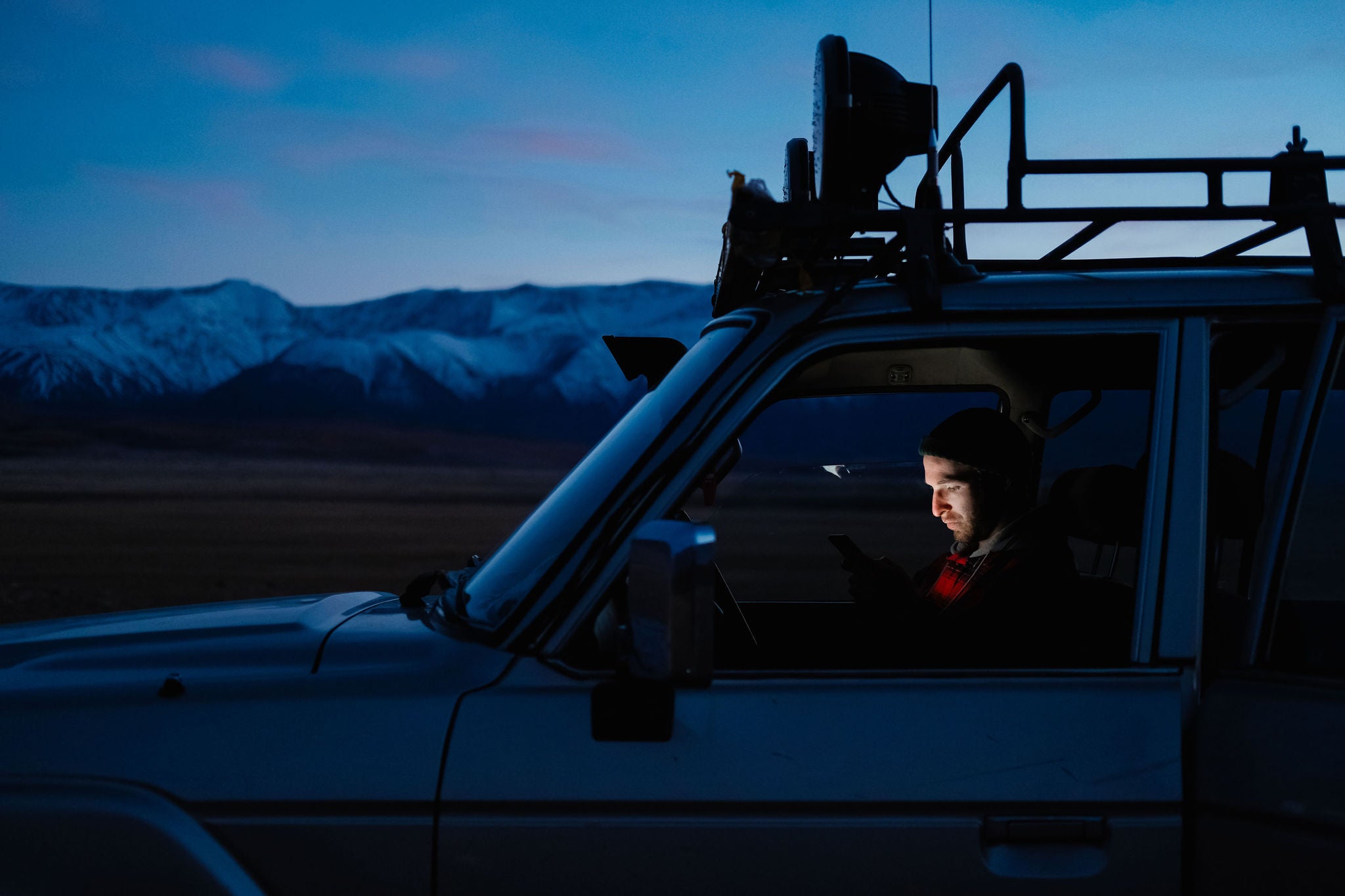 Young man using cell phone in a car at dusk.