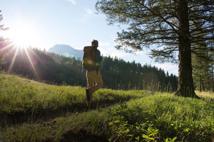 Hiker follows trail through meadow at sunrise