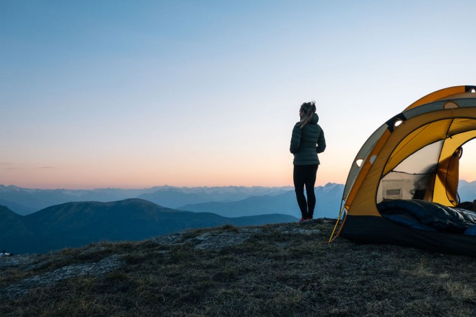 young women watches sunrise outside camping tent